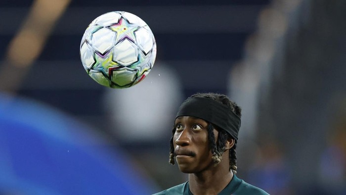 Soccer player with a black headband watches a ball spinning in the air above him in the stadium.
