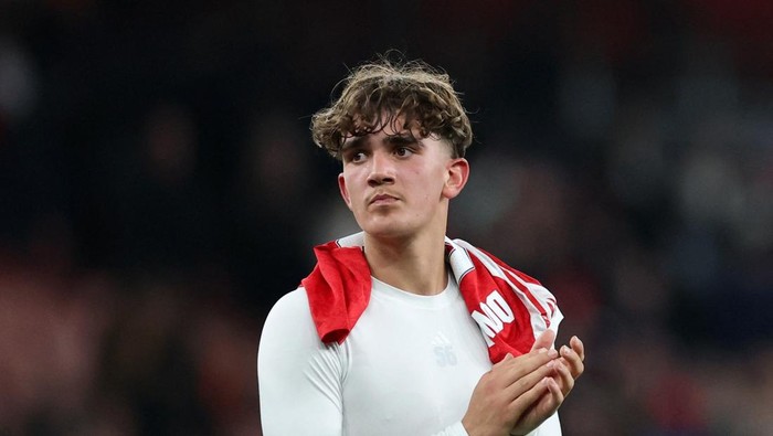 Young male athlete with a white shirt and red towel draped over his shoulders, clapping after a game.