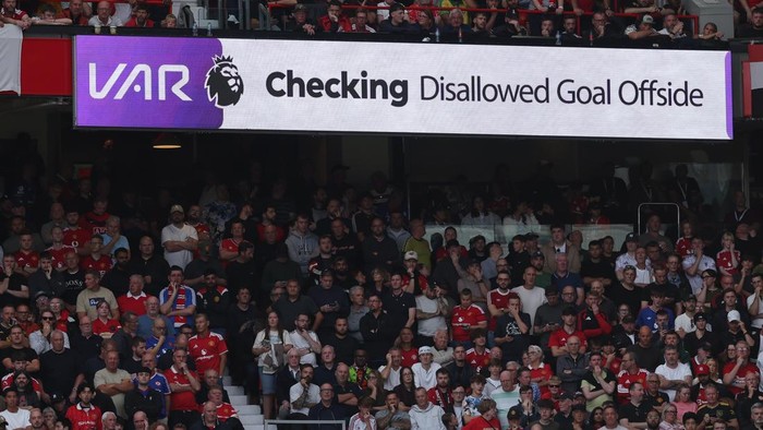 Football stadium crowd beneath a VAR banner that reads 'Checking Disallowed Goal Offside'.