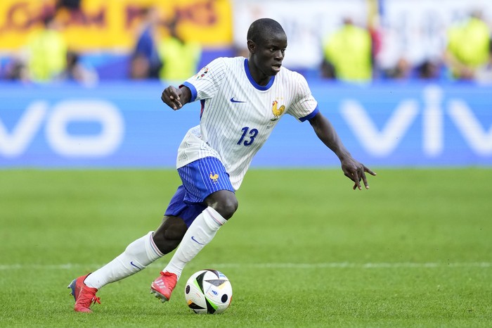 Soccer player in a white and blue kit (number 13) dribbling a ball on a green field during a match.