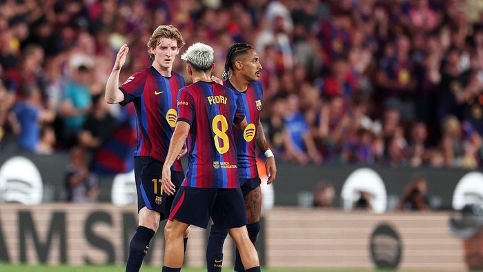 Three soccer players in red-and-blue striped jerseys celebrate on the field in a crowded stadium.