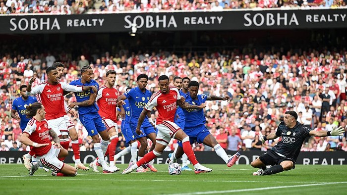 Soccer match moment: Arsenal (red) and Chelsea (blue) players contest a shot near the goal as the keeper dives to save.
