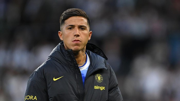 Man in a dark Chelsea jacket standing on a football pitch, looking ahead.