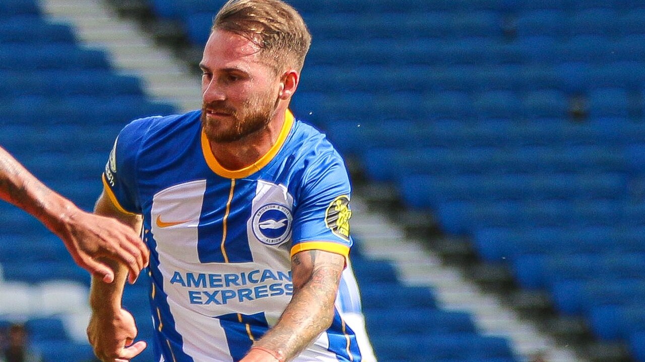 Soccer player in blue and white striped jersey sprinting on the pitch with blue stadium seats behind him.