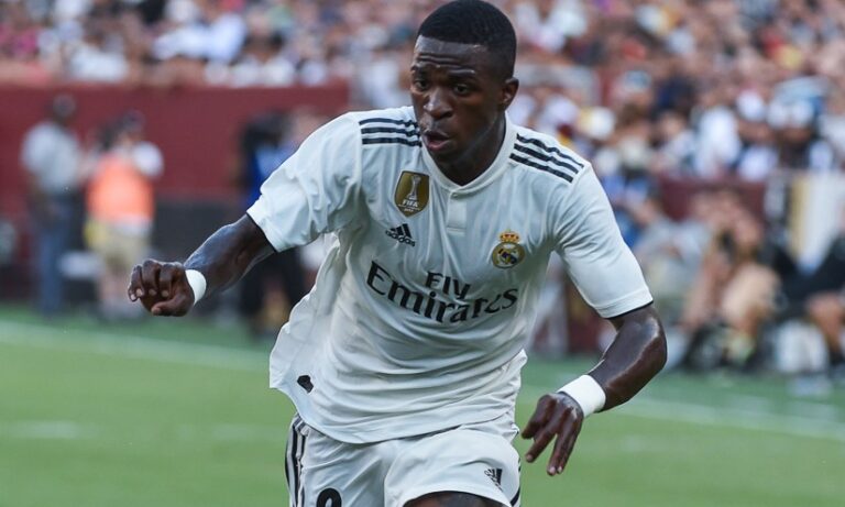 Soccer player in a white Real Madrid kit sprinting on a green field during a match.