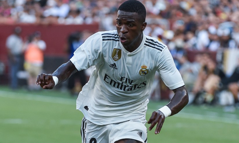 Soccer player in a white Real Madrid kit sprinting on a green field during a match.